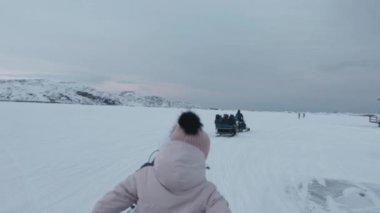 Gün batımında karlı kayaların arkasında turistli kızaklı kar arabaları. Ağır çekim. El bilgisayarı pov çekimi