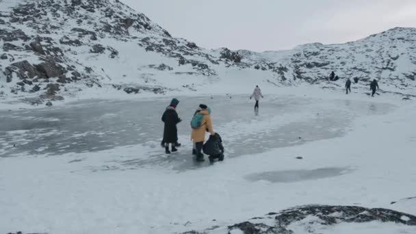 Regio Moermansk, Rusland - 10 januari 2021: Toeristen gaan over een pad tussen besneeuwde rotsen naar een bevroren reservoir voor een andere groep reizigers — Stockvideo