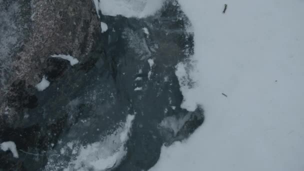 Primo piano di un ruscello d'acqua e bolle sotto ghiaccio trasparente tra la neve ai piedi della falesia — Video Stock