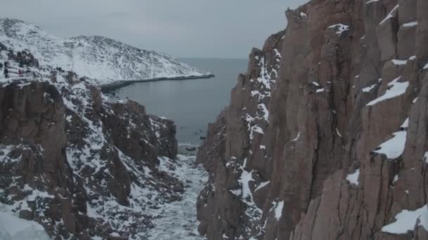 Pemandangan jurang antara batu-batu yang mengarah ke pantai dan sekelompok wisatawan di puncak tebing salju — Stok Video