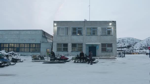Región de Murmansk, Rusia - 10 de enero de 2021: Hombres están cerca de motos de nieve en el estacionamiento a la entrada del edificio y hablan — Vídeo de stock