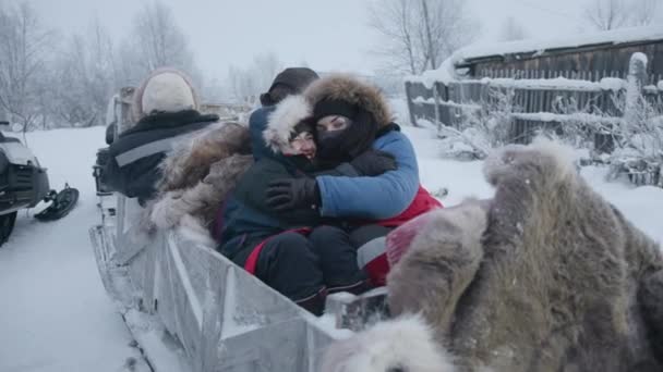 Regione di Murmansk, Russia - 10 gennaio 2021: Due ragazze sono sedute in una slitta attaccata a una motoslitta che abbraccia e ride. Rallentatore — Video Stock