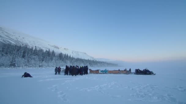 Grupa turystów stoi w pobliżu skuterów śnieżnych z saniami u podnóża góry pokrytej lasem — Wideo stockowe