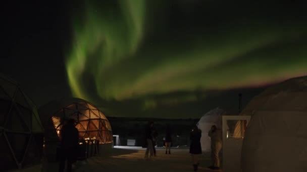 Группа туристов рядом со стеклянными иглу снимает вихри Aurora borealis на свои смартфоны. Timelapse — стоковое видео