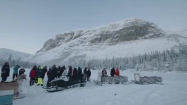Murmansk bölgesi, Rusya - 10 Ocak 2021: Bir grup turist, karlı bir dağın eteğinde kızaklı bir kar aracının yanında durup sohbet ediyorlar