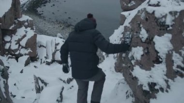 Genç bir adam uçurumun kenarında duruyor ve Barents Denizi kıyısındaki ejderha yumurtaları plajının manzarasına hayran. Arka plan