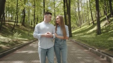 Birbirine aşık bir çift, yeşil tepeler arasında parkın patikaları boyunca kol kola gider ve birbirine bakarak konuşur. Yavaş çekim