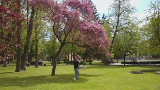 Молодий чоловік тримає свою кохану в руках і співає з нею під квітучим деревом в парку поруч з фонтаном. Повільний рух — стокове відео