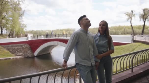 Ein romantisches junges Paar steht am Geländer der Böschung vor der Kulisse einer Bogenbrücke. Zeitlupe — Stockvideo