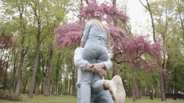 Een jonge man houdt zijn geliefde in zijn armen en wervelt met haar in de buurt van een bloeiende boom. Geluk en vreugde concept. Langzame beweging — Stockvideo