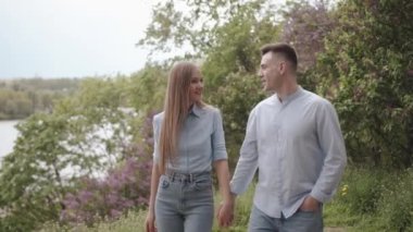 Birbirine aşık bir çift, yeşil tepeler arasında parkın patikaları boyunca kol kola gider ve birbirine bakarak konuşur. Yavaş çekim