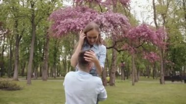 Genç bir adam sevgilisini kollarına alır ve çiçek açan bir ağacın yanında onunla birlikte döner. Mutluluk ve neşe kavramı. Yavaş çekim