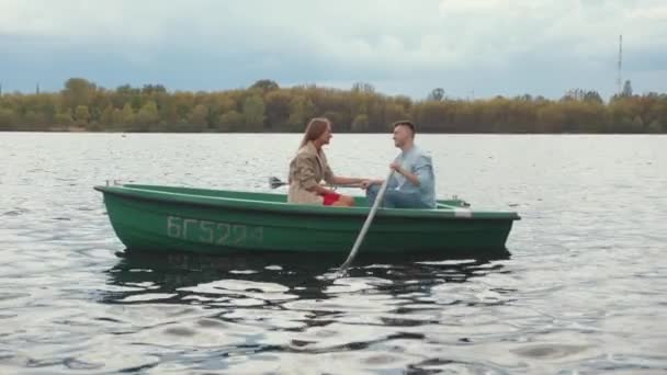 En ung man och en vacker ung flicka rider en roddbåt på sjön under en romantisk promenad. Långsamma rörelser — Stockvideo