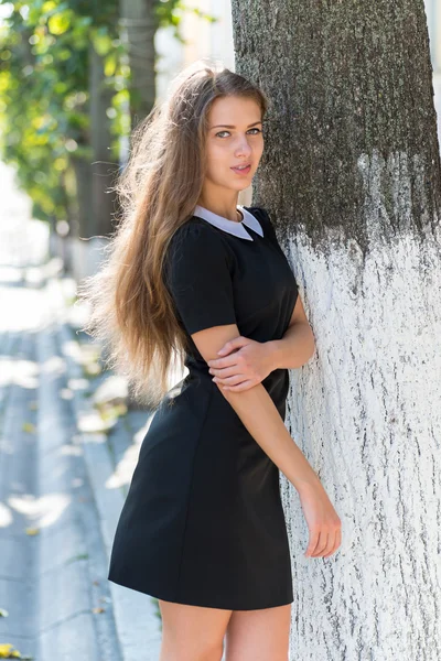 Portrait of glamorous girl in black dress standing near tree — Stock Photo, Image