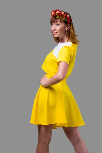 Vrouw in gele jurk met rode krans geïsoleerd op grijs — Stockfoto