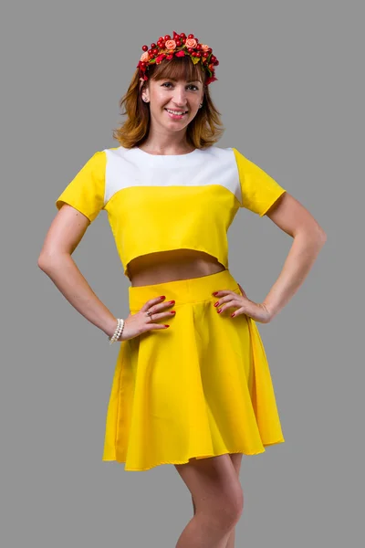 Vrouw in gele jurk met rode krans geïsoleerd op grijs — Stockfoto