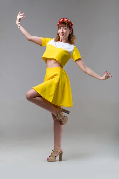 Woman in yellow dress with red wreath dancing on gray — Stock Photo, Image