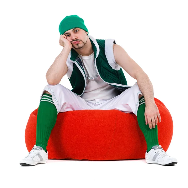 Melancholy man dressed like a gnome sitting on red bag with gifts, isolated over white — Stock Photo, Image