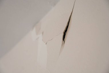 Duvardaki derin bir çatlağın dramatik yakın çekim açısı hasarın derinliğini ve kırık alçının dokusunu vurguluyor..