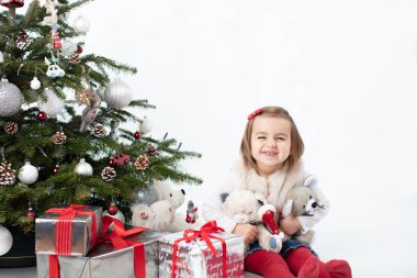 Arsız küçük kız kameraya gülümsüyor Noel ağacının yanında oturuyor