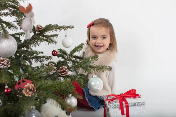 Toddler girl cheerfully playing behind Christmas tree — Stock Photo, Image