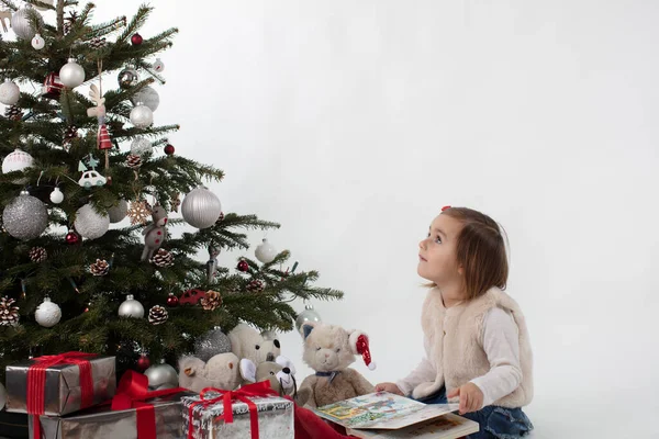 Sweet toddler girl dreaming about Christmas whilst reading a book to her soft friends — Stock Photo, Image