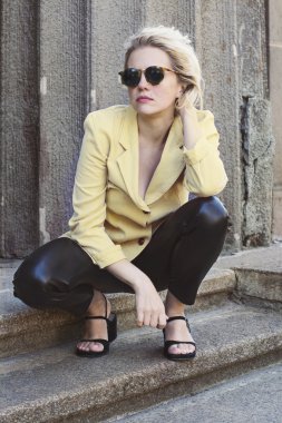 Sokakta yürüyen güzel bir genç bayan açık portresi. Gözlük, şık sarı ceket ve bir sırt çantası modeli. Kadın moda kavramı. Şehir hayatı. Güneşli gün.