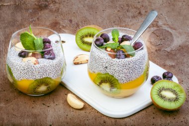Hindistan cevizi sütlü chia tohumu pudingi. Taze meyve, mango püresi, kivi parçaları, Brezilya fındığı ve naneli. Ahşap arka planda güzel bir cam.