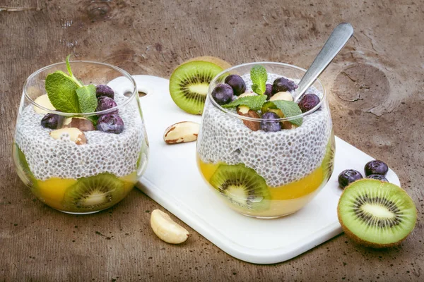 chia seed pudding with coconut milk. With fresh fruit, mango puree, kiwi chunks, brazil nuts and mint. Beautiful glass on wooden background