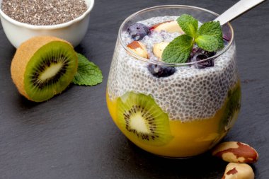 Chia, mango ve kivi tohumlu puding cam bir bardakta, seçici odak. Siyah bir arkaplanda