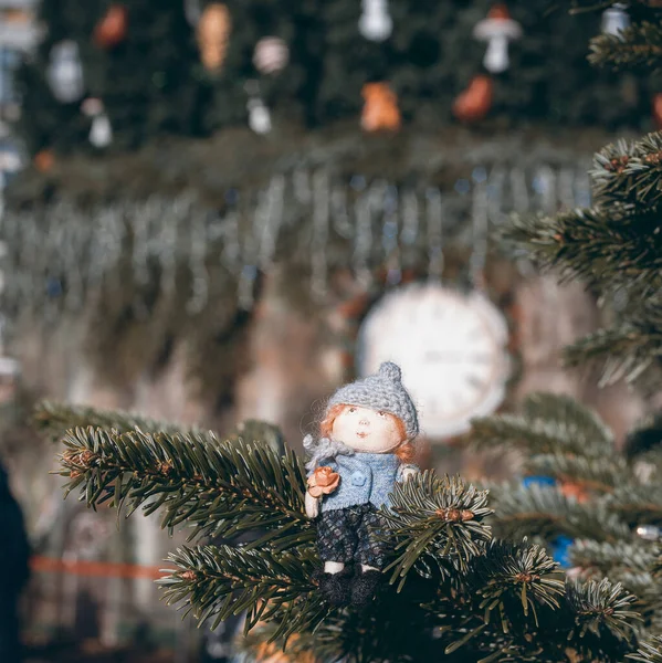 Little handmade doll on the Christmas tree with blurry view of the Christmas tree. Making a Christmas gift doll for children. Close up view of handmade doll with accessories. High quality photo