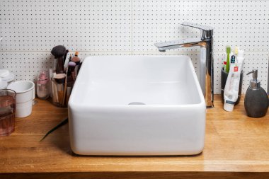 KIEV, UKRAINE - Ocak 05, 2021: Kare seramik lavabo ve ahşap tezgahın üzerindeki parlak krom musluk. Banyo içi.