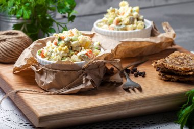 Olivier salatası, beyaz bir tabakta, havlunun üzerinde, beyaz bir kesim tahtasının üzerinde, ahşap bir arka planda.