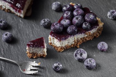 Siyah taştan bir tahtanın üzerinde yaban mersinli tofu peynirli kek. Sağlıklı vejetaryen gıda kavramı.