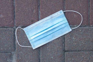 Asfalt yola atılmış kullanılmış bir cerrahi maske. Yakın plan. Maske takmama konsepti.