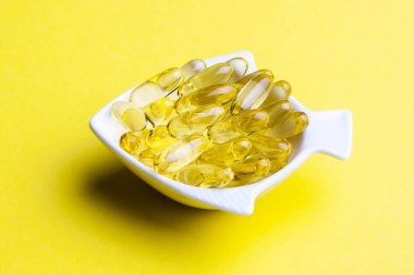 Morina yağı kapsülleri sarı arka planda balık şeklinde düzenlenir.