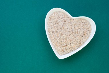 Yeşil arka planda bir fincanda psyllium tohumları kabuğu