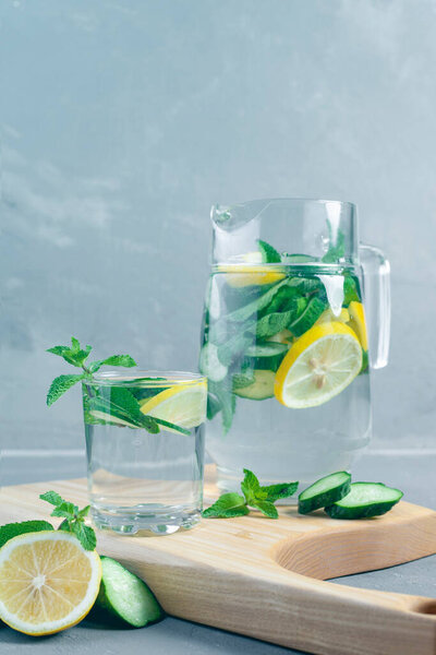 Delicious cold summer lemonade with cucumber and mint in stone jars on a light slate, stone or concrete background.