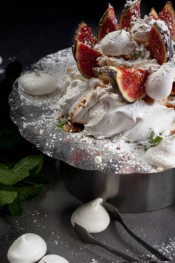 Siyah arkaplanda tatlı. Anna Pavlova 'nın krem şanti ve taze incirle kaplı kreması, üzerine pudra şekeri ve fıstık cipsi serpiştirilmiş, yakın plan, uzay kopyası.