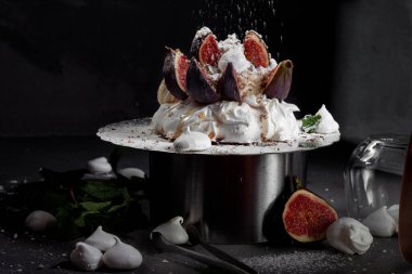 Siyah arkaplanda tatlı. Anna Pavlova 'nın krem şanti ve taze incirle kaplı kreması, üzerine pudra şekeri ve fıstık cipsi serpiştirilmiş, yakın plan, uzay kopyası.