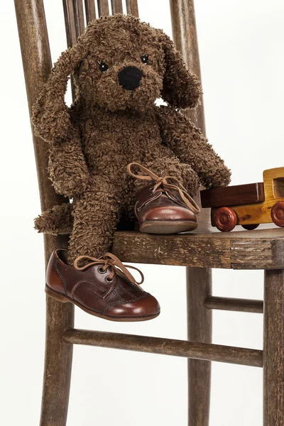 Bonito cachorrinho de brinquedo macio sentado em uma cadeira em sapatos de couro velhos — Fotografia de Stock