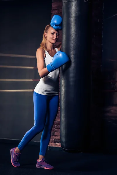 Женщина, прислонившаяся к боксерской сумке в синих боксерских перчатках — стоковое фото