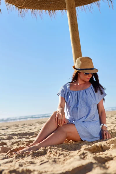 Anne adayı güneş şemsiyesinin altında kuma oturur.