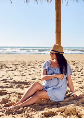 Anne adayı güneş şemsiyesinin altında kuma oturur.