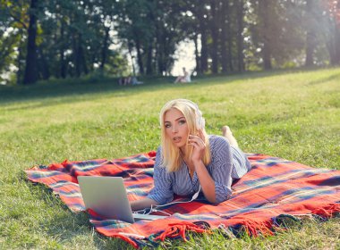 Çayır üzerinde kulaklık ile dizüstü bilgisayar kullanan mutlu kız