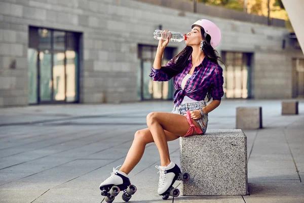 Young woman on roller skates and helmet drinking water — ストック写真