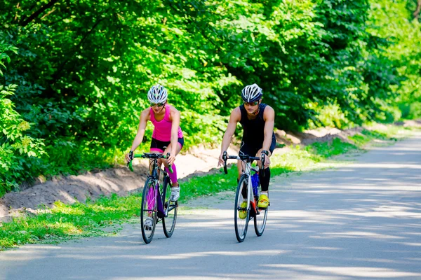 Jovem par de ciclistas profissionais andando na estrada — Fotografia de Stock