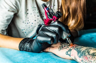 Master tattoo draws orange paint on clients hand clipart