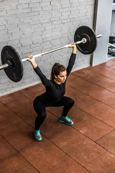 Vrouw opleiding squats met halters over hoofd — Stockfoto