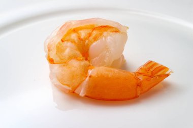 Yakın plan pişmiş kuyruklu pembe karides beyaz tabakta.